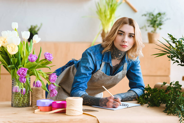 young florist taking notes and looking at camera at workplace - Foto, Bild