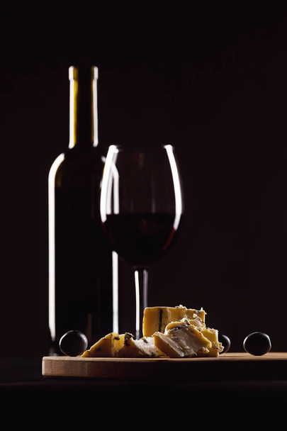 wine glass and bottle, cheese with mold  and grapes on black background - Fotó, kép