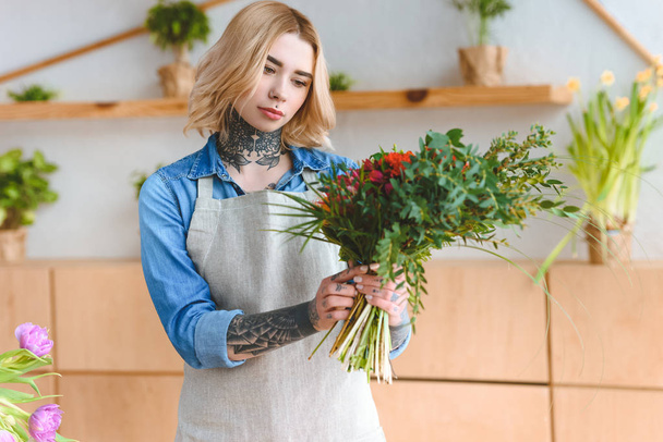 attractive young tattooed woman in apron holding beautiful bouquet in flower shop - 写真・画像
