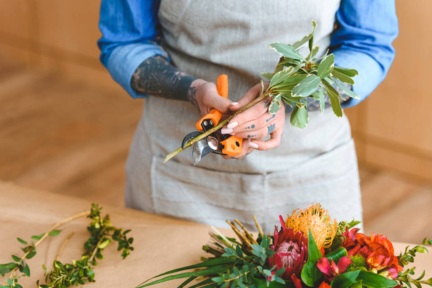 mid section of young florist in apron cutting plants at workplace - Photo, Image