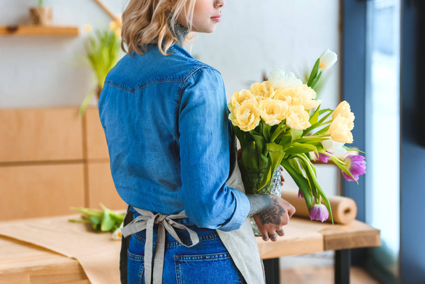 back view of young florist holding beautiful tulips in vase - Photo, Image