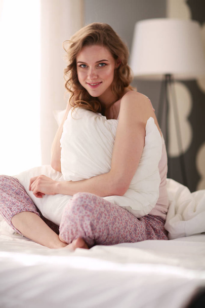 Young woman holding a pillow while sitting on her bed - Photo, Image