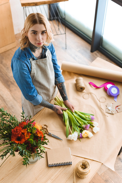 high angle view of young florist arranging flowers and looking at camera  - Photo, Image
