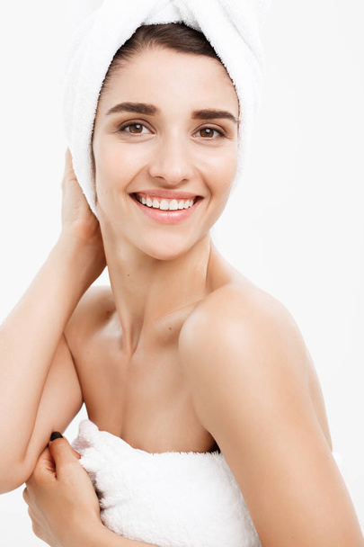 Ομορφιά και το δέρμα φροντίδα έννοια - όμορφη Καυκάσιος νεαρή γυναίκα με πετσέτα στο κεφάλι που καλύπτει το στήθος της, στο λευκό που αγγίζει το δέρμα της. - Φωτογραφία, εικόνα