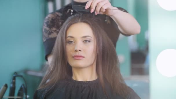 Professional hairstylist creating evening hairstyle for attractive smiling model - Footage, Video