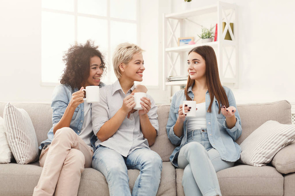 Three young female friends with coffee chatting at home - Fotó, kép
