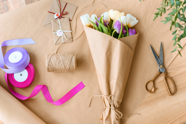 top view of beautiful bouquet of tulips, scissors, ribbons and envelopes with rope on craft paper - Photo, Image
