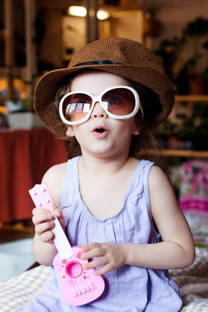 Malá holka kluk baví s kytarou hračku v ruce a sluneční brýle na obličej - Fotografie, Obrázek