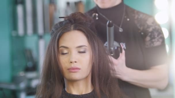 Hairstyle master creating evening hairstyle for attractive female model - Footage, Video