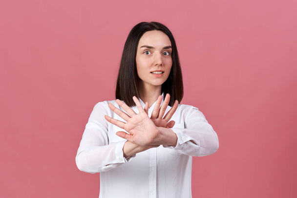 a young white-skinned brunette in a white shirt pulls her hands and crossed palms in front of her - Foto, immagini