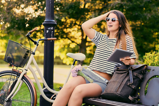 Portrait of an attractive brunette sits on a bench with bicycle  - Foto, afbeelding