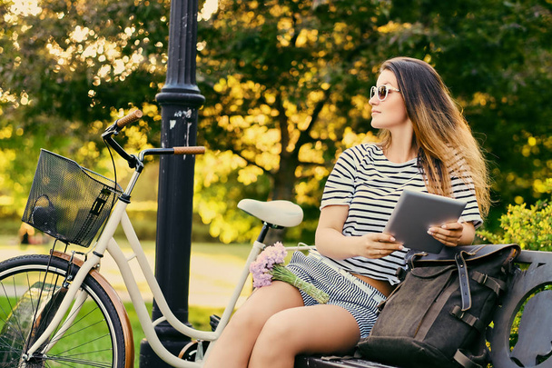 Egy vonzó barna portréja ül egy padon, kerékpár  - Fotó, kép