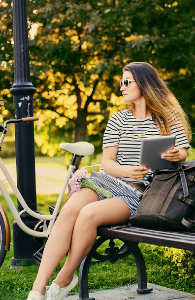 Portrait of an attractive brunette sits on a bench with bicycle  - Photo, image