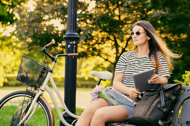Retrato de una atractiva morena sentada en un banco con bicicleta
  - Foto, imagen