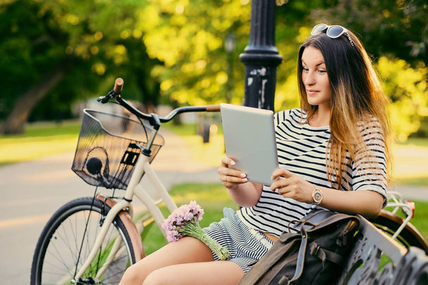 Портрет привлекательной брюнетки сидит на скамейке с велосипедом
  - Фото, изображение