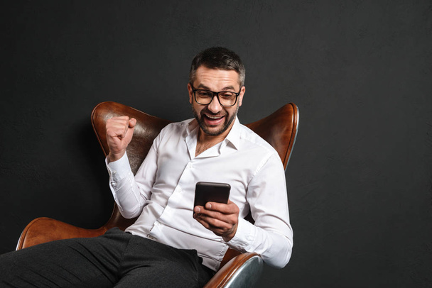 Excited businessman sitting using mobile phone. - Φωτογραφία, εικόνα