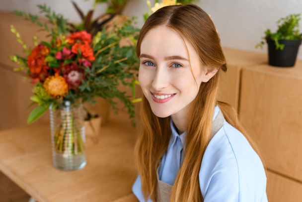 portrait of beautiful young female florist smiling at camera in flower shop - Zdjęcie, obraz