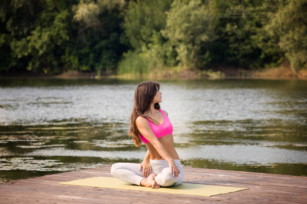 Young girl practices yoga on the shore of the lake, the concept of enjoying privacy and concentration, sunlight - Photo, Image