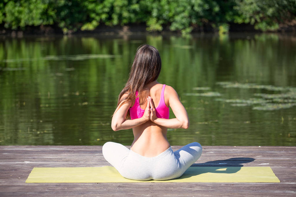 Young girl practices yoga on the shore of the lake, the concept of enjoying privacy and concentration, sunlight - Photo, Image
