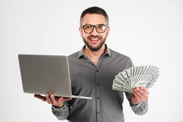Happy businessman using laptop computer holding money. - Foto, immagini