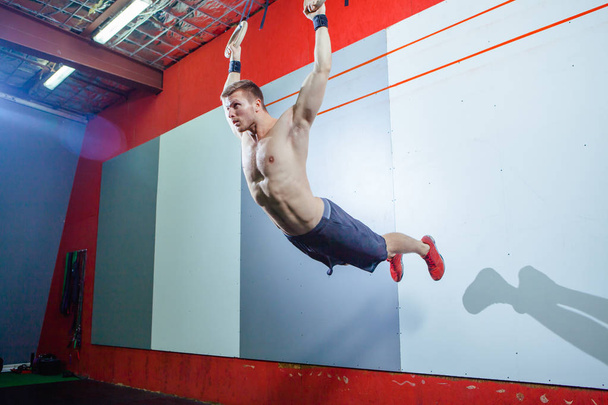 Muscle-up exercise young man doing intense cross fit workout at the gym on gymnastic rings. - Φωτογραφία, εικόνα