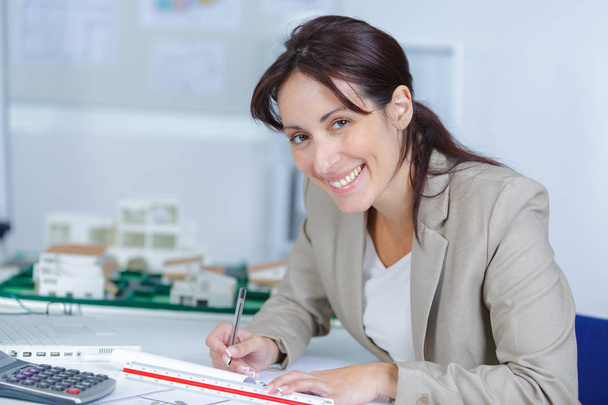 beautiful young smiling female sitting at the desk and writing - Foto, Imagen