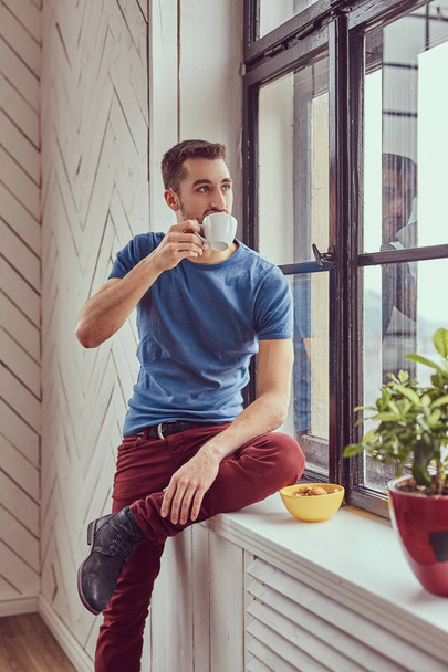 Młody student kaukaski pije poranną kawę siedząc na windo - Zdjęcie, obraz