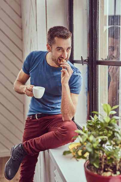 Young caucasian student drinks morning coffee sitting on a windo - Фото, зображення
