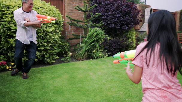 Family of four are having a water fight in the garden with water pistols. - Πλάνα, βίντεο