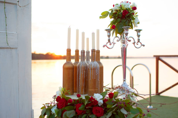 Свадебный декор - красивая инсталляция за столом у моря: свечи, бутылки, статуэтка
 - Фото, изображение