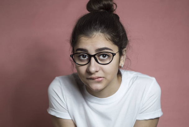 A thoughtful girl in glasses looks at the camera. A young woman thinks about the idea by biting her lower lip. - Fotoğraf, Görsel