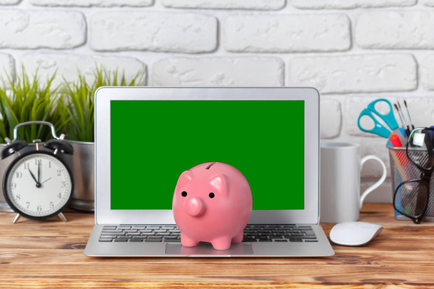 Piggy money box with laptop on wooden table - Foto, afbeelding