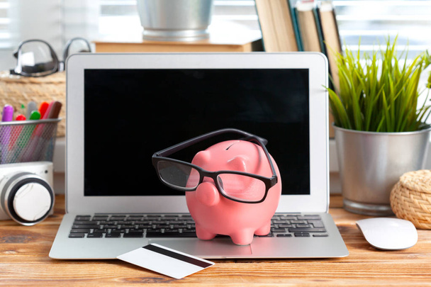 Piggy money box with laptop on wooden table - Foto, afbeelding
