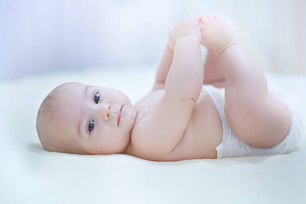 Cute kid playing with his feet in a sunny bedroom - Photo, image