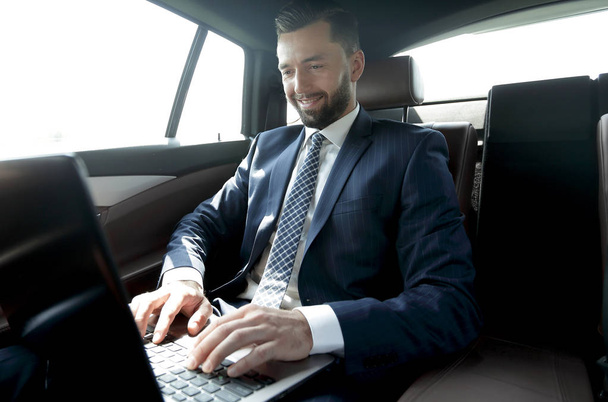 businessman sitting in the back-seat of a car, using his laptop - 写真・画像