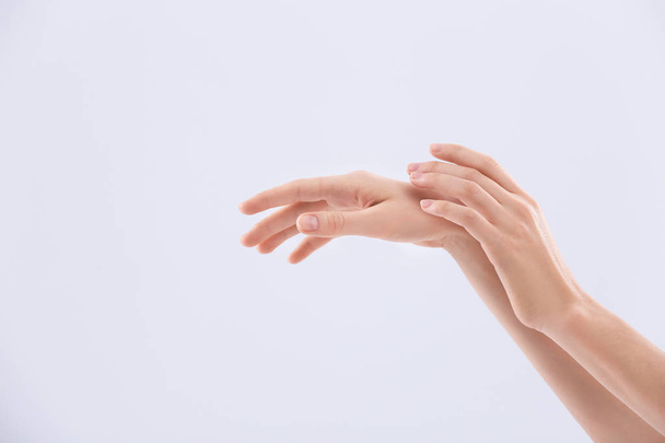 Mujer joven aplicando crema en las manos sobre fondo claro
 - Foto, Imagen