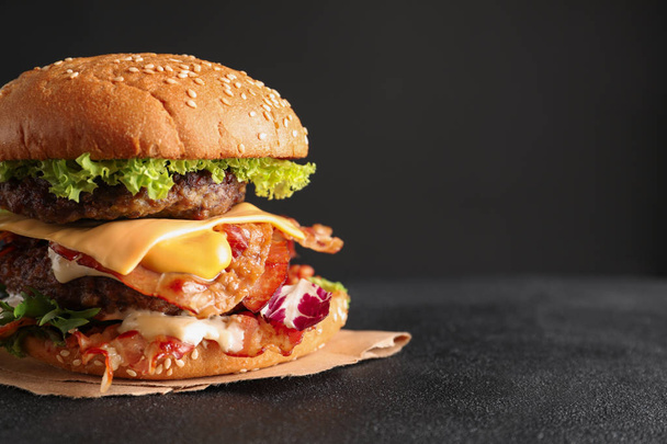 Tasty double burger with bacon on table against dark background - Photo, image