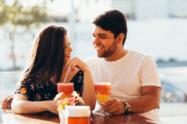 Young couple in love sitting in a restaurant, drinking colorful drink, having a conversation and enjoying the time spent with each other - Photo, image
