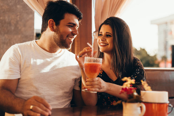 Young couple in love sitting in a restaurant, drinking colorful drink, having a conversation and enjoying the time spent with each other - Фото, изображение
