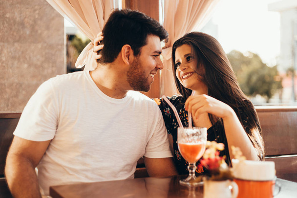 Young couple in love sitting in a restaurant, drinking colorful drink, having a conversation and enjoying the time spent with each other - Fotografie, Obrázek