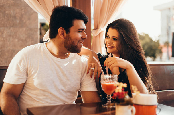 Mladý pár v lásce, posezení v restauraci, pití barevné nápoje, konverzaci a užívat si čas strávený s sebou - Fotografie, Obrázek