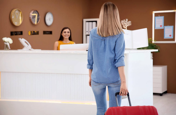 Young woman with luggage near reception desk in hotel - Foto, Imagen
