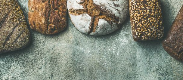 Various bread selection. Top view of Rye, wheat and multigrain rustic bread loaves over grey background - Photo, Image
