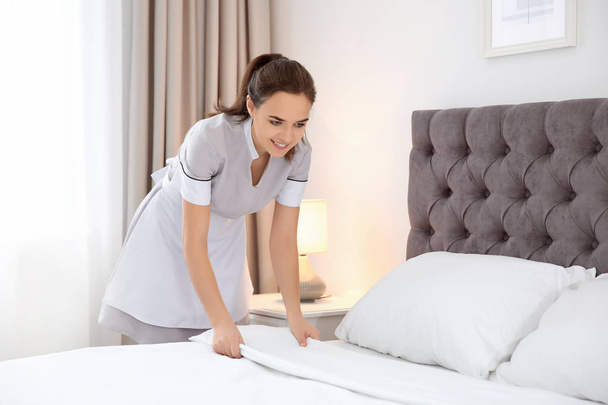 Young maid making bed in hotel room - Foto, Imagem