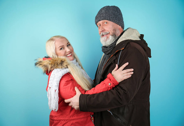 Ouder paar in warme kleding op kleur achtergrond. Klaar voor de wintervakantie - Foto, afbeelding