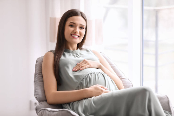 Young pregnant woman resting in armchair at home - Foto, immagini