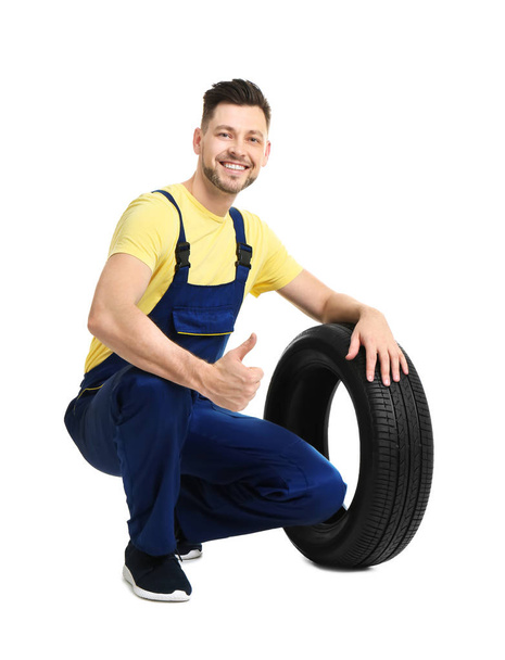 Male mechanic with car tire on white background - Foto, afbeelding