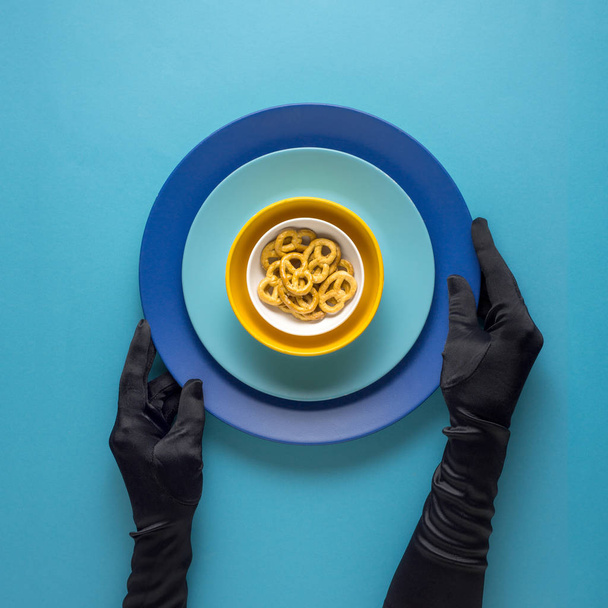 Creative concept photo of kitchenware with hand, painted plate with food on it on blue background. - Photo, Image