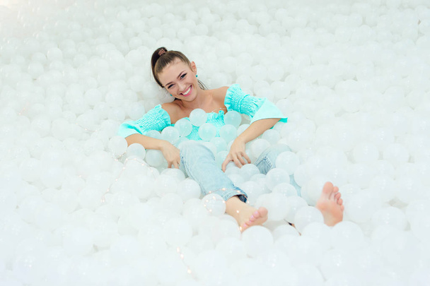 Happy beautiful woman lays surrounded by white plastic balls in the dry pool for adult. - 写真・画像