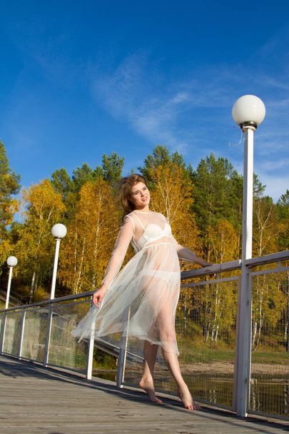 girl in a transparent white dress is standing on a wooden bridge - Fotó, kép